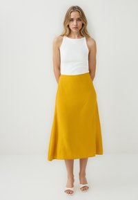 Gonna midi gialla a forma A in un materiale morbido, abbinata a un top bianco aderente senza maniche. Design semplice con minimi dettagli e texture morbida.