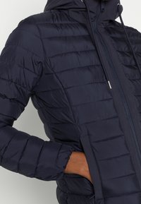 Marineblauwe donzen jas met doorgestikt design, voorzien van een capuchon, ritssluiting en elastische manchetten. Gestructureerde stof met een gladde afwerking.