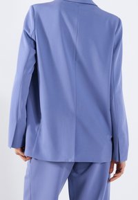 Lichtblauwe blazer met een soepele textuur, enkele vent aan de achterkant en een getailleerde pasvorm, gecombineerd met bijpassende broek.