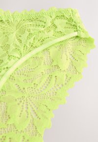 Neoonroheline lilleline pitskangas laineliste servade ja õhukese elastse paelaga heleda tausta vastu.