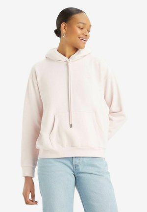 Sudadera de color rosa claro hecha de tela suave, con un bolsillo delantero, capucha con cordón y puños acanalados. Combinada con unos jeans de color azul claro.