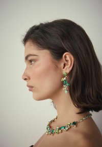 Grüne und türkisfarbene Edelsteinohrhänger mit goldfarbener Hardware, die verschiedene Formen und Größen aufweisen. Passende Edelsteinkette mit goldenen Akzenten.