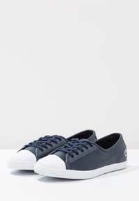 Marinblå snörskor med vit gummitå och sula, i slät syntetisk material och med en liten logotyp på sidan.