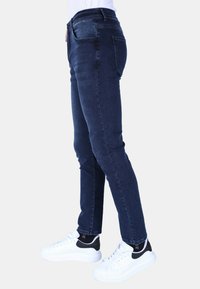 Donkerblauwe spijkerbroek met een slim fit, middelhoge taille en vijf zakken, gecombineerd met witte sneakers met zwarte accenten.