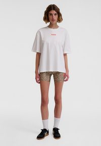 Hvid bomulds T-shirt med "hummel"-logo i rødt. Bruges med tan leopardmønstrede shorts. Sorte sneakers og hvide mellemlange sokker fuldender looket.