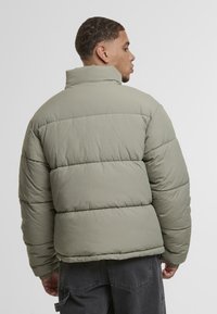 Olivengrønn puffer-jakke med høy krage og quiltet mønster, med en avslappet passform og elastiske mansjetter, laget av lett materiale.