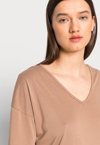 T-shirt castanho com decote em V, feita de um tecido macio e com um corte relaxado. Mangas curtas e textura suave. Design minimalista, adequado para uso casual.