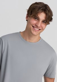 Szara koszulka z krótkim rękawem wykonana z miękkiego materiału, z okrągłym dekoltem. Gładka faktura bez wzorów i widocznych akcentów.