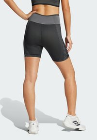 Pantaloni da ciclismo neri a vita alta con accenti grigi, texture a coste e motivo a strisce diagonali lungo i fianchi. Scarpe da ginnastica bianche visibili.