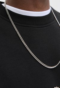 Sudadera negra con un cuello alto, que presenta un interior blanco y un collar de cadena plateada que cae por delante.