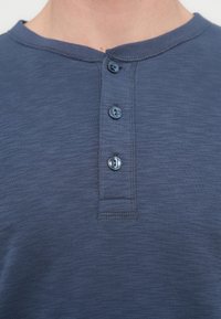 Μπλε ναυτικό πουκάμισο henley με απαλή υφή, που διαθέτει στρογγυλό λαιμόκοψη και τρία στρογγυλά κουμπιά. Ορατή ραφή κατά μήκος των άκρων.