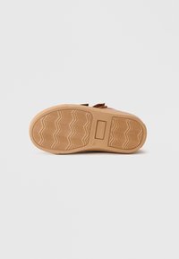 Suela de calzado con un diseño de goma texturizada en beige, con patrones en zigzag y un acento rectangular en el lateral.