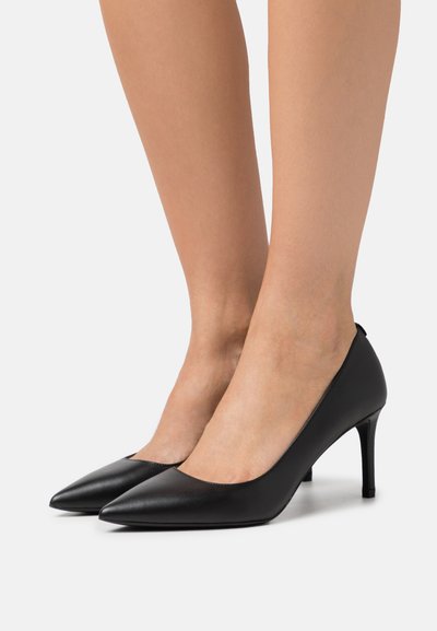 Chaussures à talons hauts en cuir noir avec un design à bout pointu, texture lisse et un talon fin de 10 cm, arborant un style minimaliste.