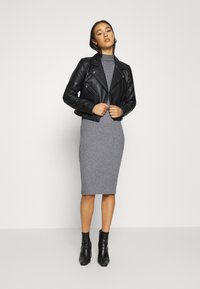 Schwarze Leder-Bikerjacke über einem grauen gerippten Midikleid, kombiniert mit schwarzen Knöchel-Stiefeln. Die Jacke hat Reißverschlüsse und Schulterklappen.