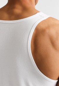 Biały bezrękawnik z miękkiego materiału, z okrągłym dekoltem i szerokimi armholes, prezentujący gładką strukturę i staranne szwy.