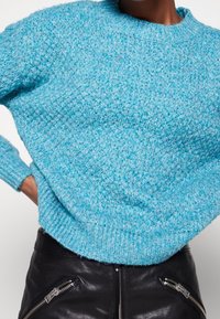 Ljusblått texturerat tröja med rund halsringning och ribbade manschetter, kombinerat med åtsittande svarta läderbyxor med dragkedjeaccenter.