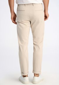 Pantaloni beige con una vestibilità slim e orli arrotolati, realizzati in un tessuto liscio. Presentano due tasche posteriori e sono abbinati a sneakers bianche.