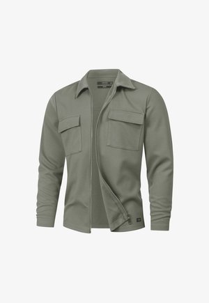 Olijfgroene blouse met lange mouwen en een ritssluiting aan de voorkant, twee borstzakken en een klassieke kraag. Zachte stof met een gestructureerd oppervlak.