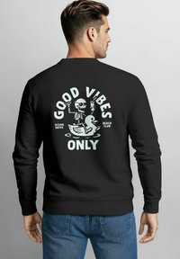 Schwarzer Sweatshirt mit Grafik auf der Rückseite, die ein Skelett und eine Ente zeigt, Text mit der Aufschrift "NUR GUTE VIBES", lässige Passform mit langen Ärmeln.