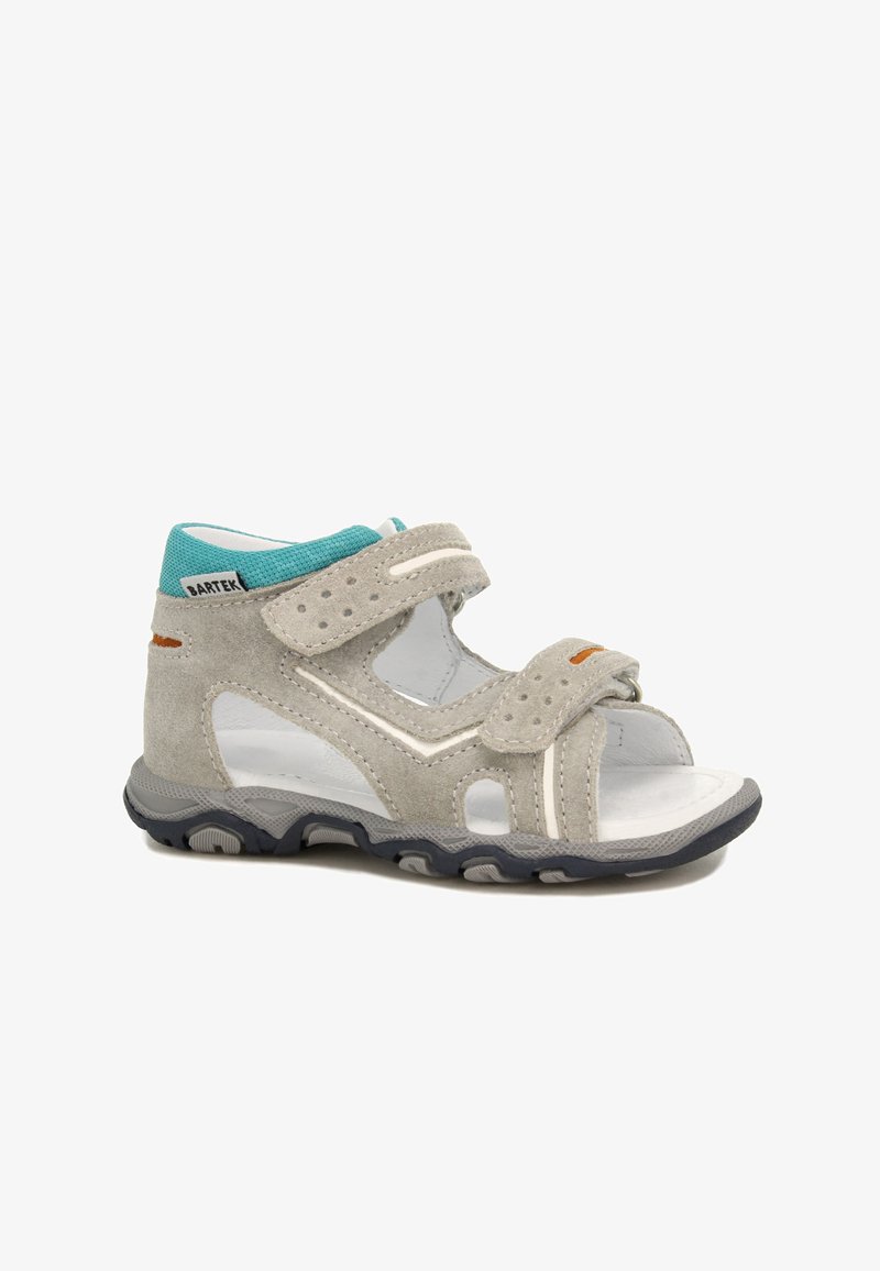 Světle šedá semišová sandál s nastavitelnými suchými zipy, výřezovými detaily a tyrkysovým akcentem na límci. Disponuje texturovanou gumovou podrážkou.