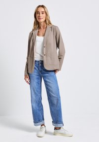 Beige kavaj med två framfickor och enkel knappstängning, parat med ljusblå vida jeans och vita sneakers. Enkel vit topp under.