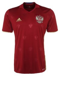 Röd fotbollsdräkt i slät tyg, med ett subtilt präglat mönster av örnar, guldakcent och en Adidas-logga på bröstet.