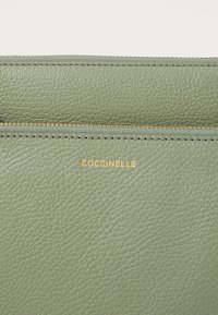 Portafoglio in pelle verde texturizzata con logo dorato "Coccinelle" e zip contrapposta con dettagli dorati.