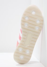 Sula med texturerad yta, i ljusrosa och vitt, med cirkulära grepplösa och vertikala spår för grepp och stabilitet.