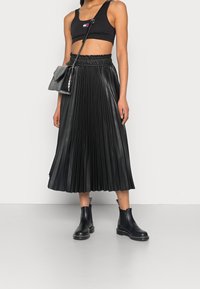 Gonna plissettata in finta pelle nera con vita elastica, abbinata a un crop top nero e stivali Chelsea neri. Accompagnata da una piccola borsa nera.