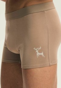 Beżowe bawełniane bokserki o gładkiej fakturze, z dekoracyjnym białym logo renifera na dolnym lewym boku.