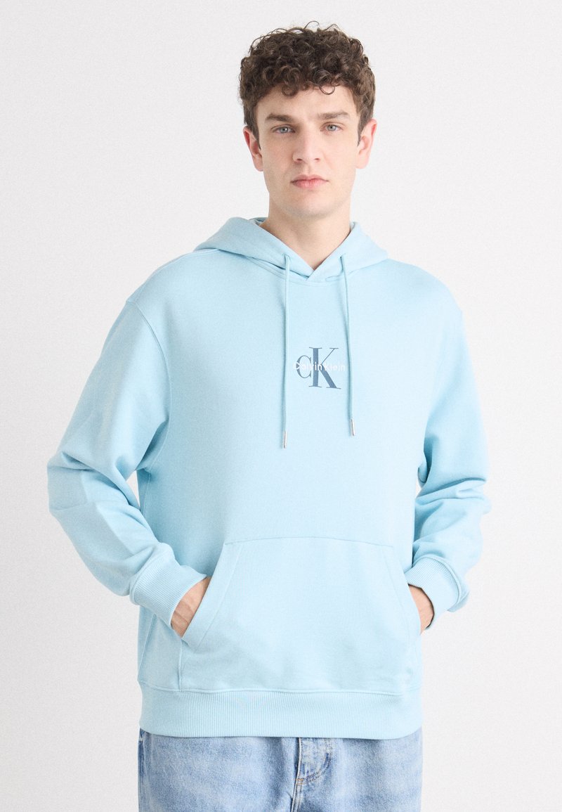 Sudadera de color azul claro con un bolsillo frontal, capucha con cordón y logo bordado "CK". Hecha de tela suave, presenta puños y dobladillo de punto acanalado.