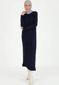 Abito lungo in maglia blu navy con texture a coste, scollatura rotonda e maniche lunghe. Abbinato a stivali crema fino al ginocchio. Design semplice ed elegante.