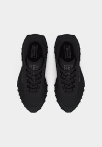 Paire de baskets noires Lacoste à lacets avec semelles robustes, présentées en vue de dessus sur un fond clair.