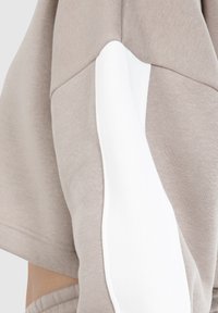 Lichtbeige sweatshirt met een witte zijpaneel, zachte textuur, oversized pasvorm, en zichtbare stiksels op de mouwen en zoom.