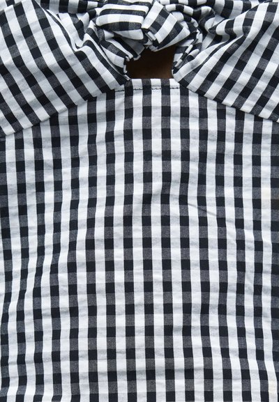 Υφασμα με ασπρόμαυρο καρό σχέδιο και έναν κόμπο στο κέντρο επάνω, δημιουργώντας ένα μικρό άνοιγμα τύπου κλειδαρότρυπας κάτω από τον κόμπο.