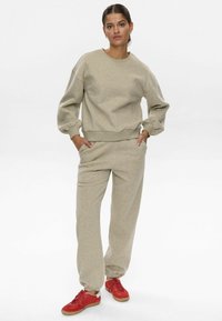 Sudadera beige y pantalones a juego en tejido suave con puños y dobladillo acanalados. Zapatillas rojas completan el atuendo, presentando un diseño clásico con cordones.