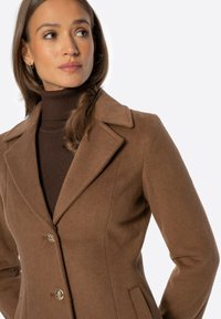 Brązowy wełniany płaszcz z klapowanym kołnierzem, dwoma przednimi kieszeniami i złotymi guzikami. Tkanina ma gładką fakturę i dopasowany krój.