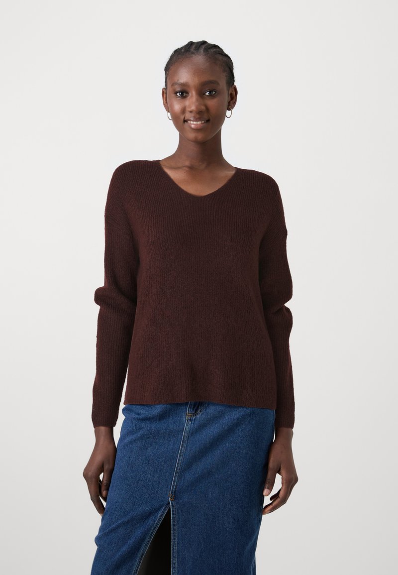 Burgunderfarbener Strickpullover mit V-Ausschnitt, langen Ärmeln und lockerer Passform, kombiniert mit einem Jeansrock mit einem vorderen Schlitz.