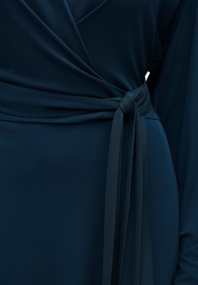 Λεπτομέρεια μίντι φόρεμα σε σκούρο μπλε χρώμα με μακριά μανίκια και δεμένη ζώνη από ύφασμα στη μέση.