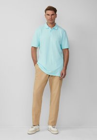 Lichtblauwe polo met een klassieke kraag, gecombineerd met beige broek en witte sneakers. Soepele stof en gestroomlijnde pasvorm.
