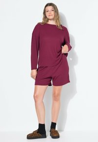 Top de manga larga de canalé burdeos combinado con pantalones cortos a juego. Tejido texturizado con un corte relajado. Llevado con calcetines negros y sandalias de estampado animal.