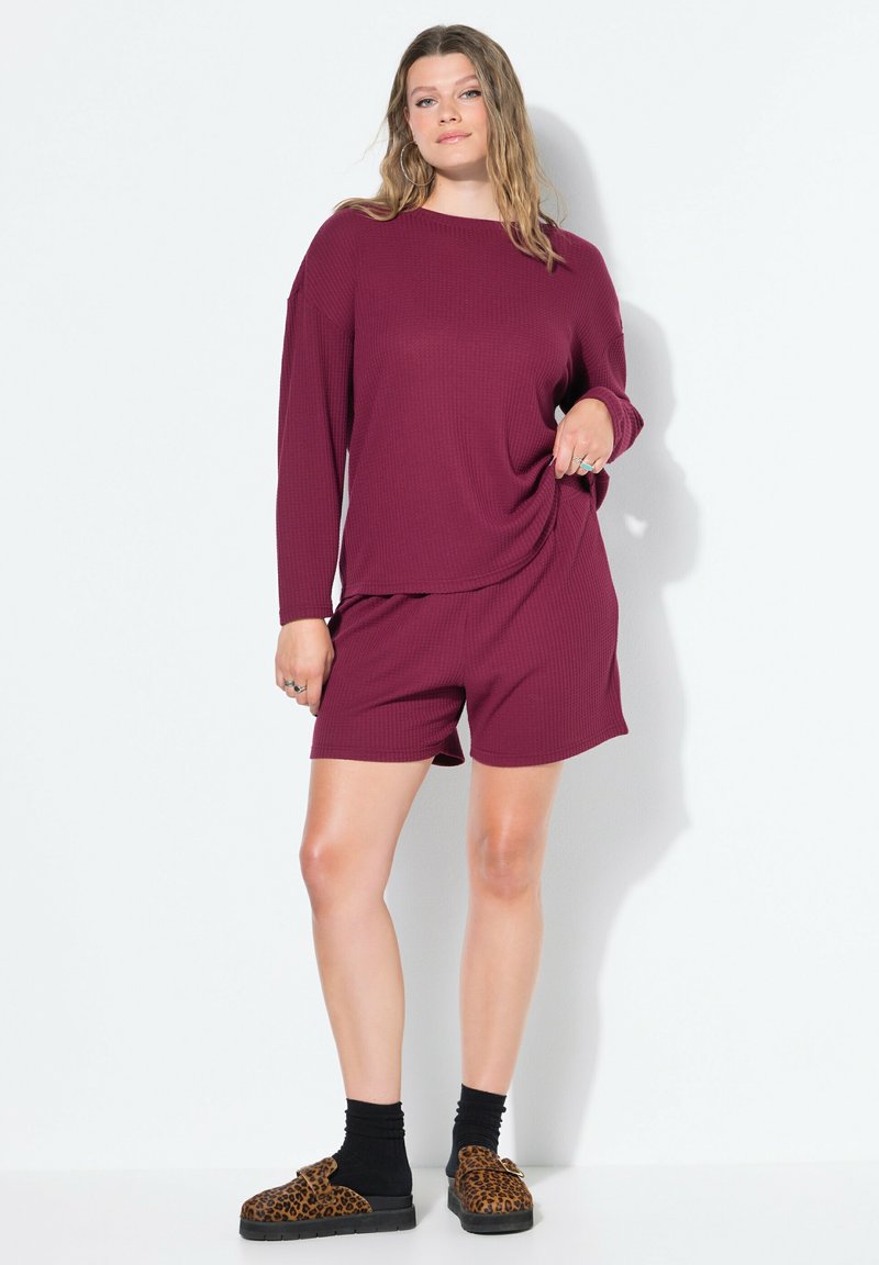 Top de manga larga de canalé burdeos combinado con pantalones cortos a juego. Tejido texturizado con un corte relajado. Llevado con calcetines negros y sandalias de estampado animal.