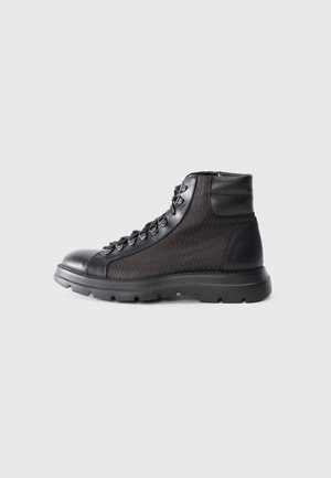 Botas de senderismo negras con un cuerpo de tela negra texturizada, punta redondeada, diseño con cordones y una suela de goma gruesa para tracción.