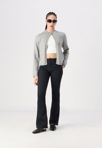 Cardigan cinza de lã com decote redondo e frente aberta, combinado com uma t-shirt branca cropped e jeans pretos de boca de sino. Sapatos planos pretos completam o visual.