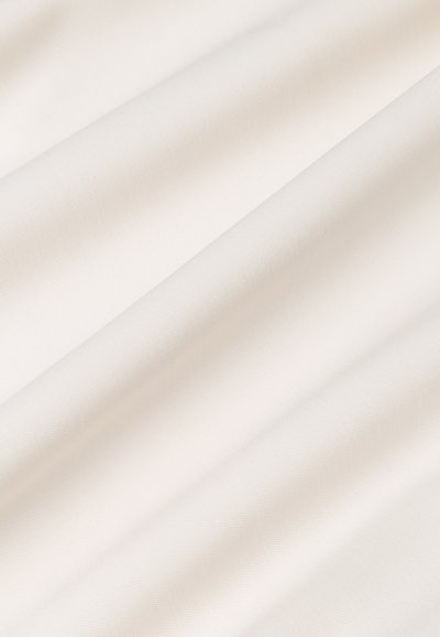 Tessuto di cotone color bianco sporco, caratterizzato da una superficie liscia con una leggera lucentezza, che scende dolcemente in pieghe, evidenziando la sua leggerezza.