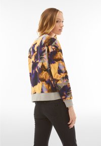 Floral-patterned bomber jacket in yellow, purple, and black tones, made of soft fabric with a gray ribbed hem and cuffs.