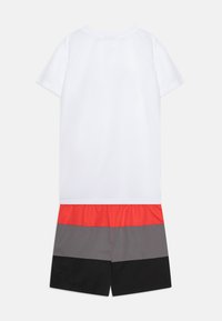 Kortärmad vit T-shirt i kombination med shorts med horisontella ränder i röd, grå och svart. Mjuk tyg, avslappnad design, elastisk midja.
