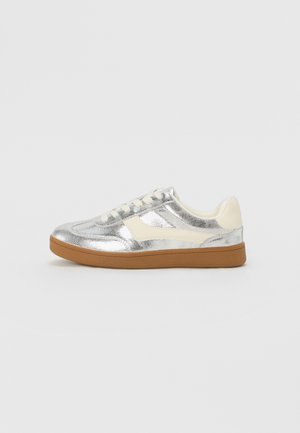 Sneaker metallico argento con accenti crema e suola in gomma marrone; presenta punte tonde, lacci e parte superiore liscia e strutturata.