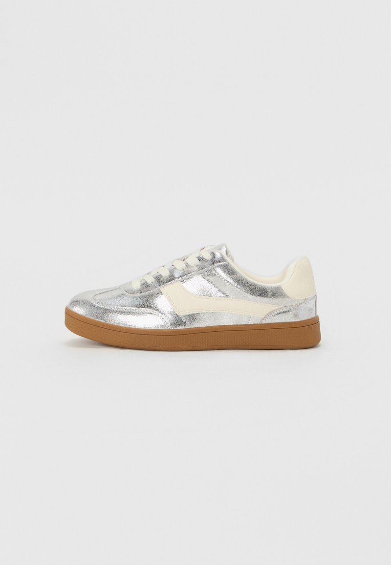 Sneaker metallico argento con accenti crema e suola in gomma marrone; presenta punte tonde, lacci e parte superiore liscia e strutturata.