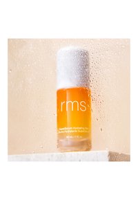Bernsteinserum in einer klaren Glasflasche mit einem weißen Deckel. Auf der Flasche sind der Markenname "rms" und Produktdetails abgedruckt. Nasser Oberflächenhintergrund.